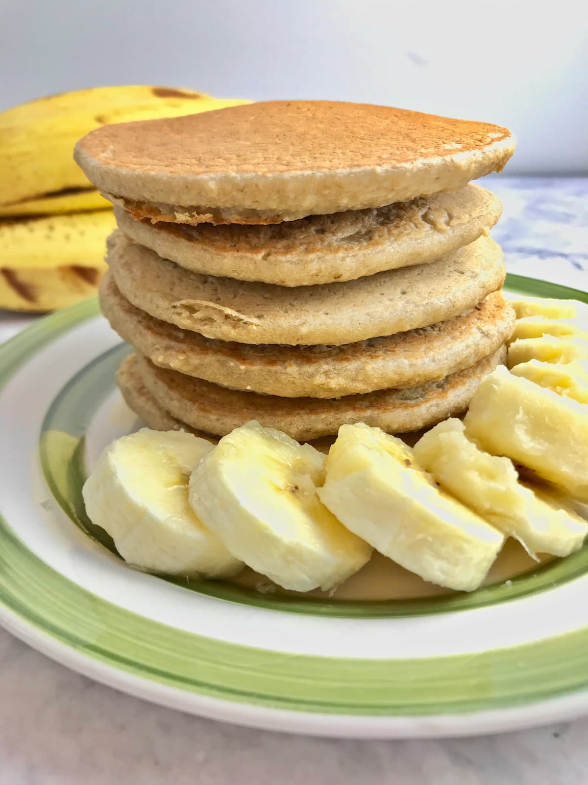 Stack of pancakes with banana slices on a plate.