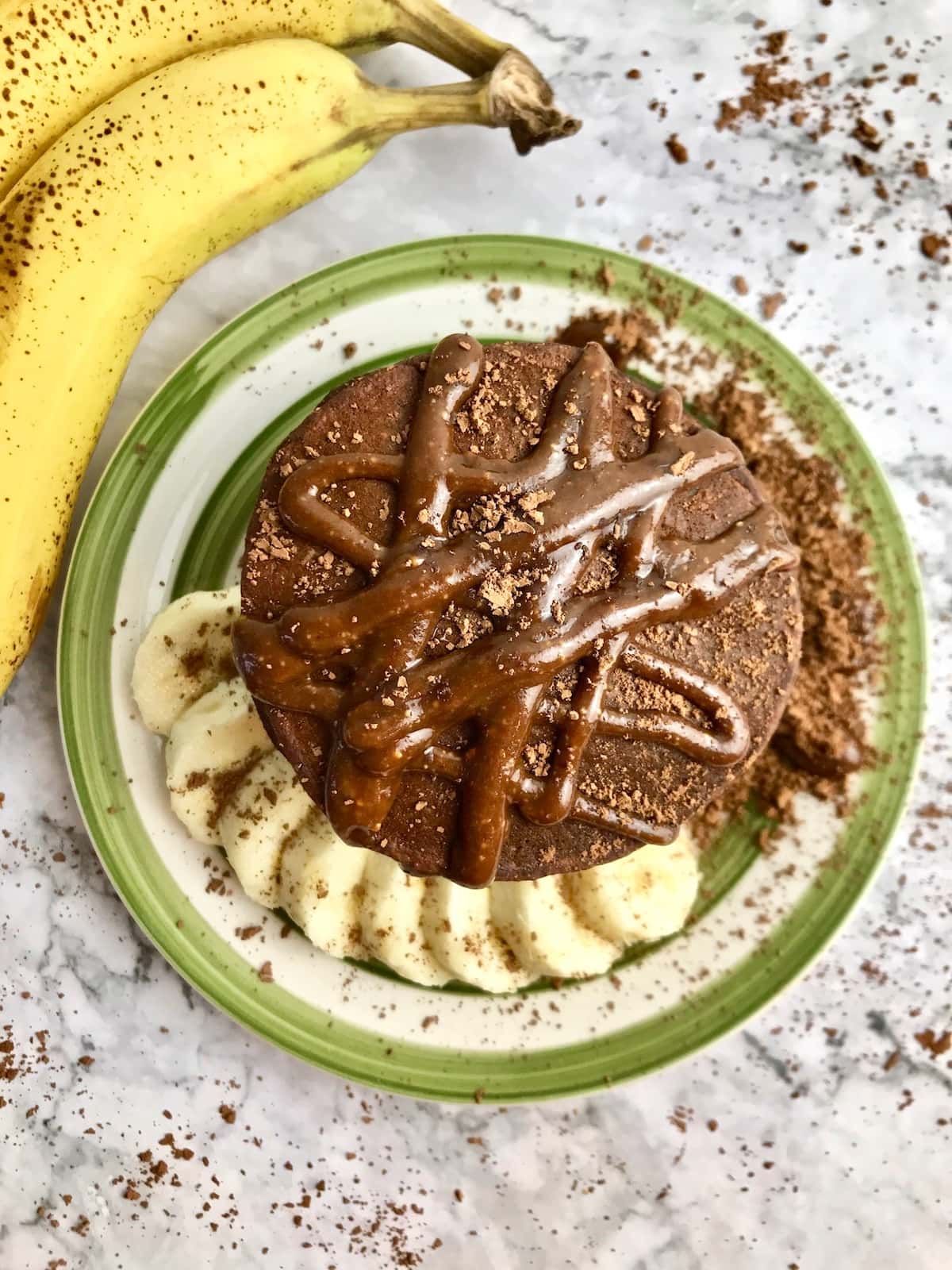 Overhead view of stack of chocolate pancakes with chocolate syrup and cacao powder sprinkled on top.