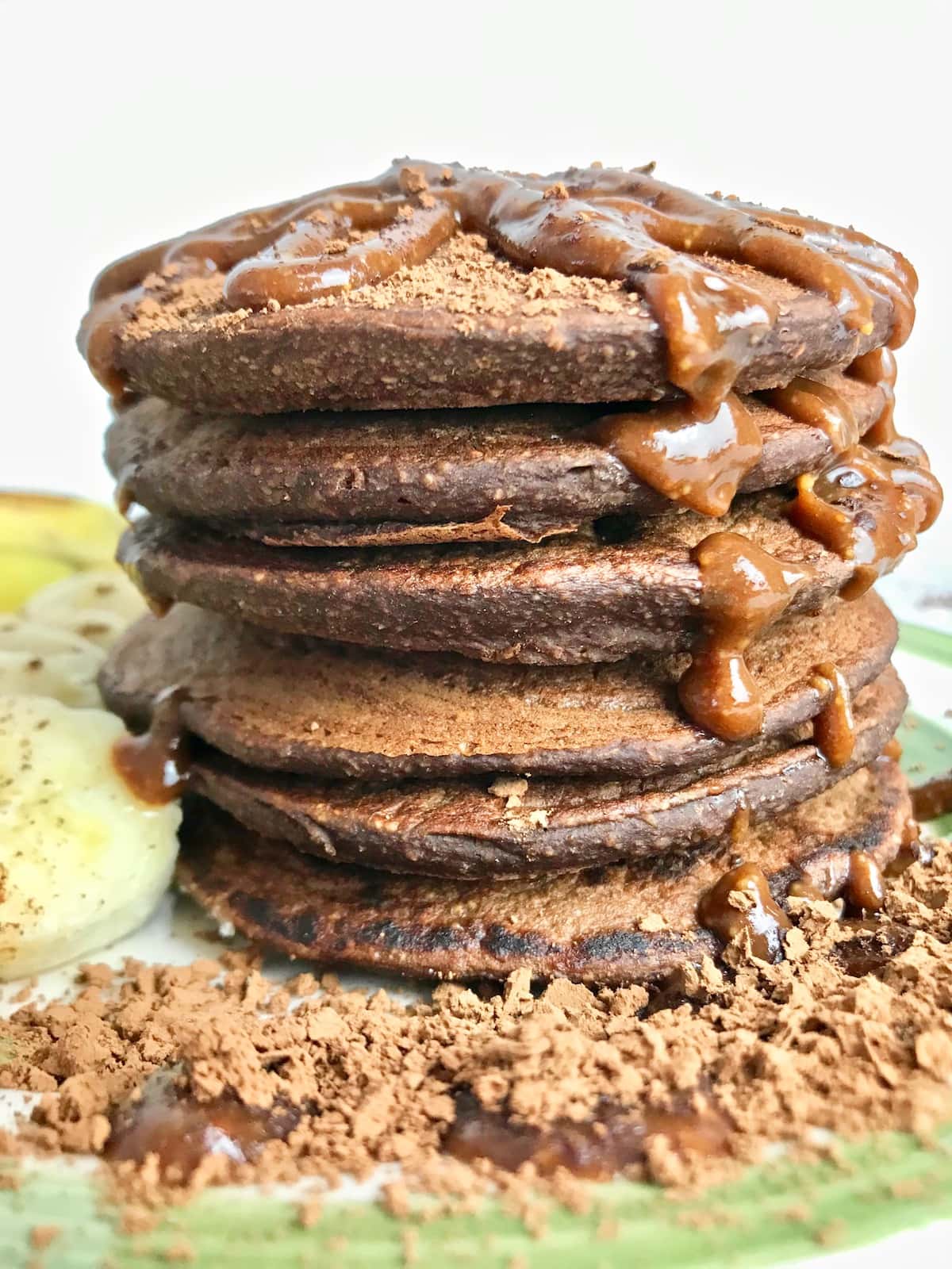 Stack of chocolate pancakes with chocolate syrup and cacao powder on top.