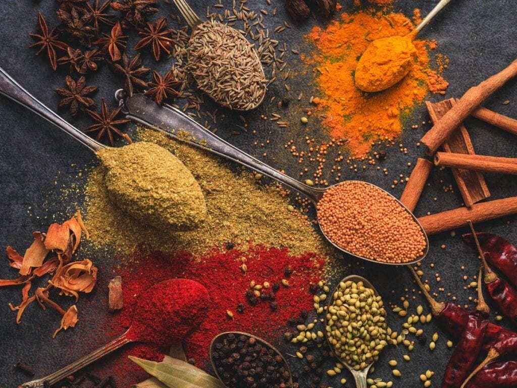 A variety of spices on spoons. Includes red, yellow, and orange powdered spices.