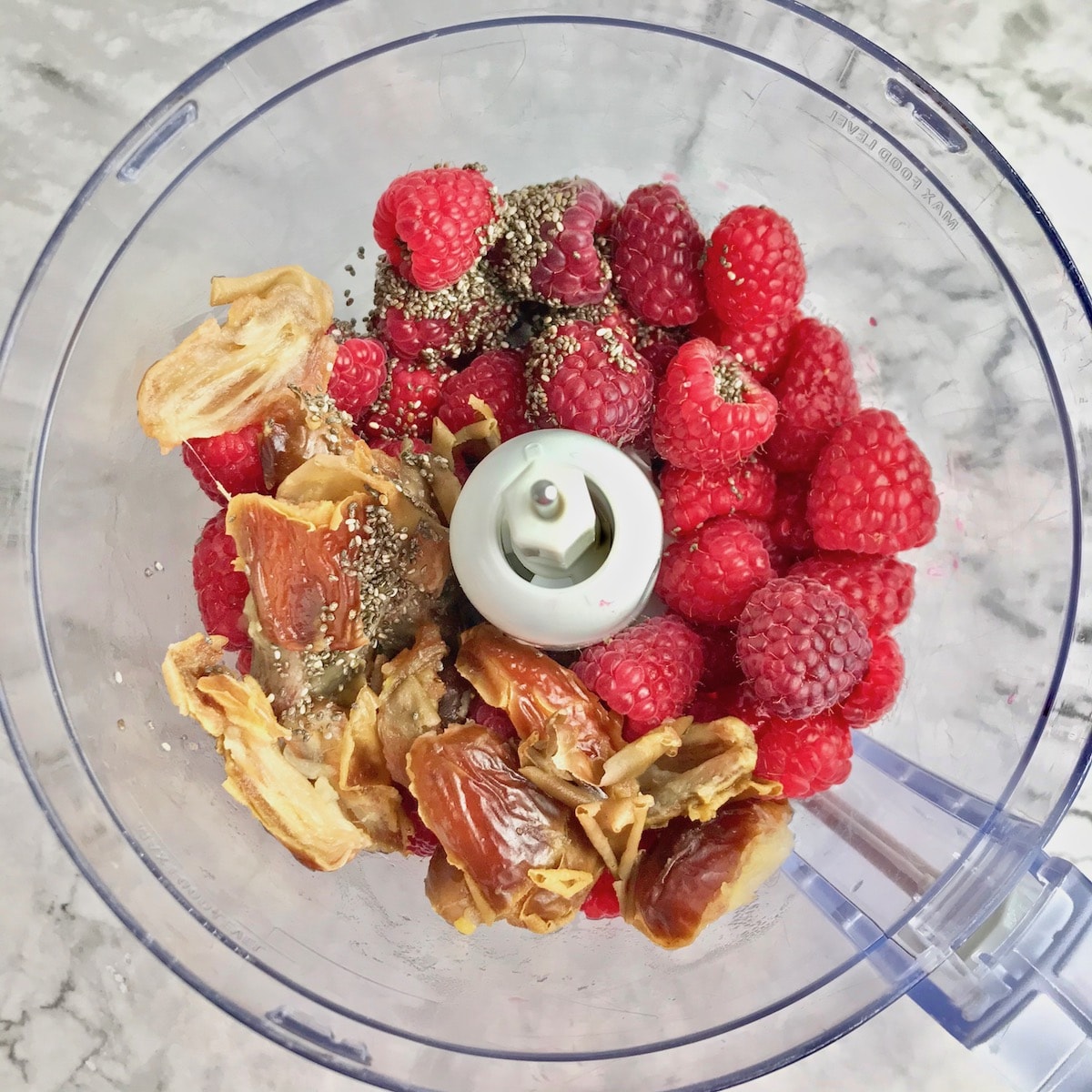 Raspberries, dates, and chia seeds in a food processor.
