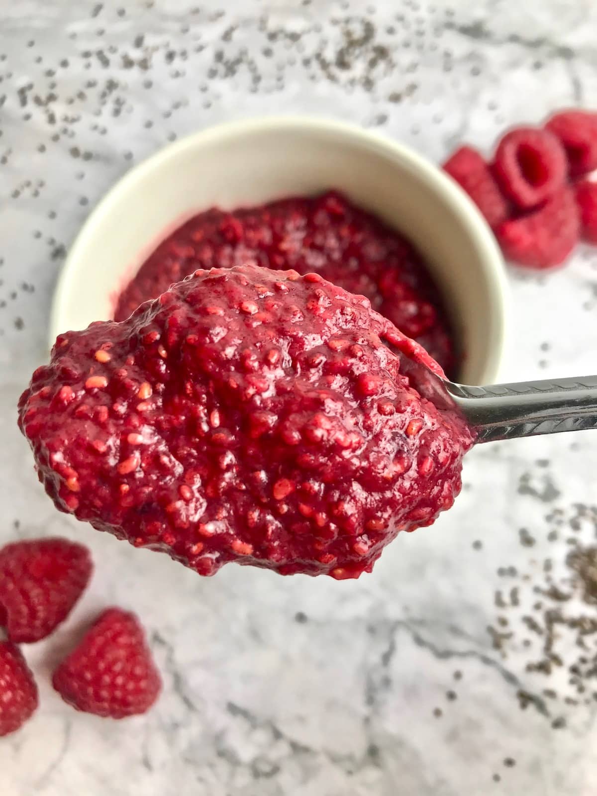 Spoonful of jam with raspberries and chia seeds on the table in the background.