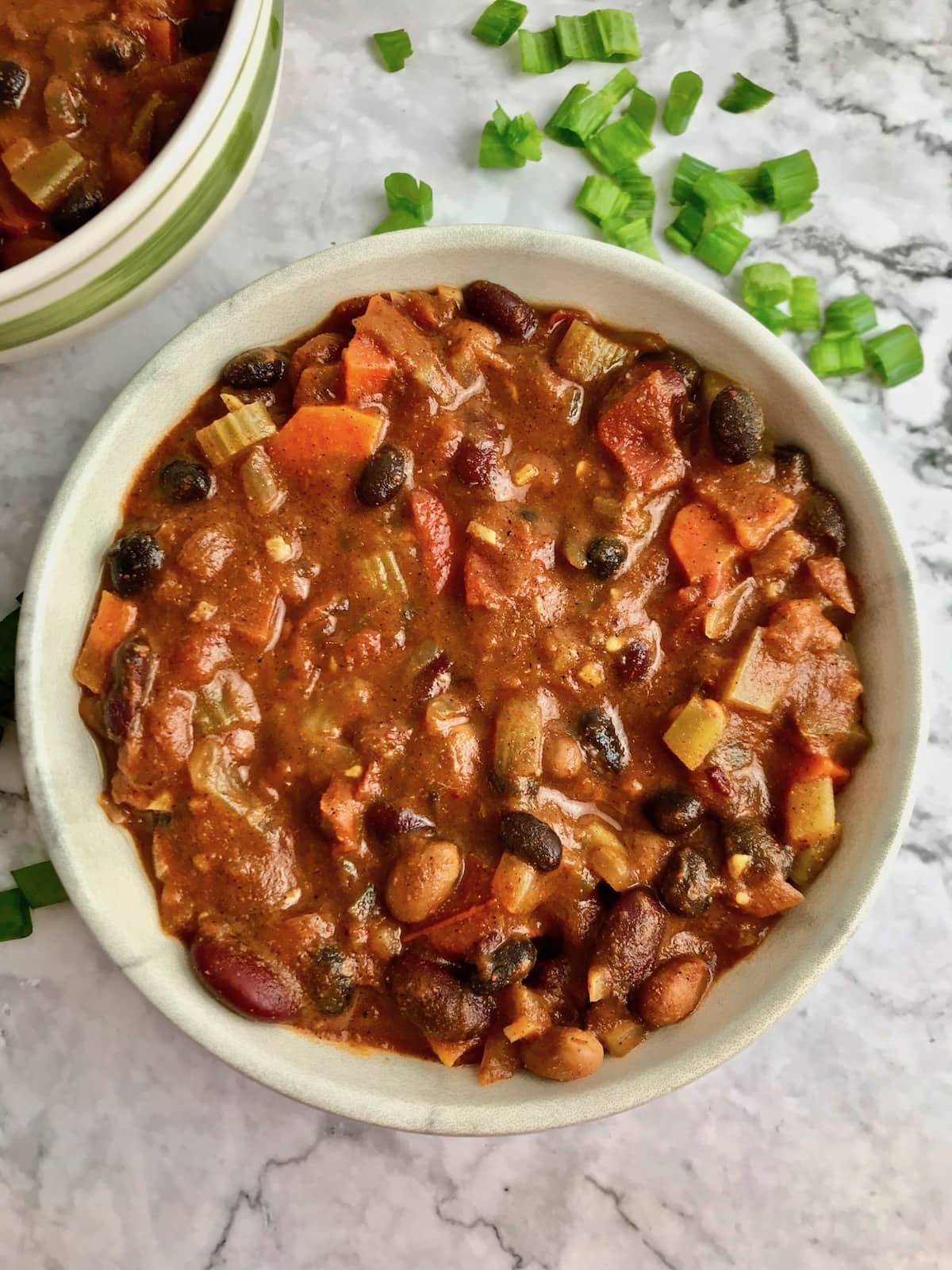 A bowl of veggie and bean chili on a table with chopped green onion.