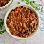 A bowl of vegan bean chili on a table with chopped green onion.