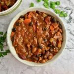 A bowl of vegan bean chili on a table with chopped green onion.