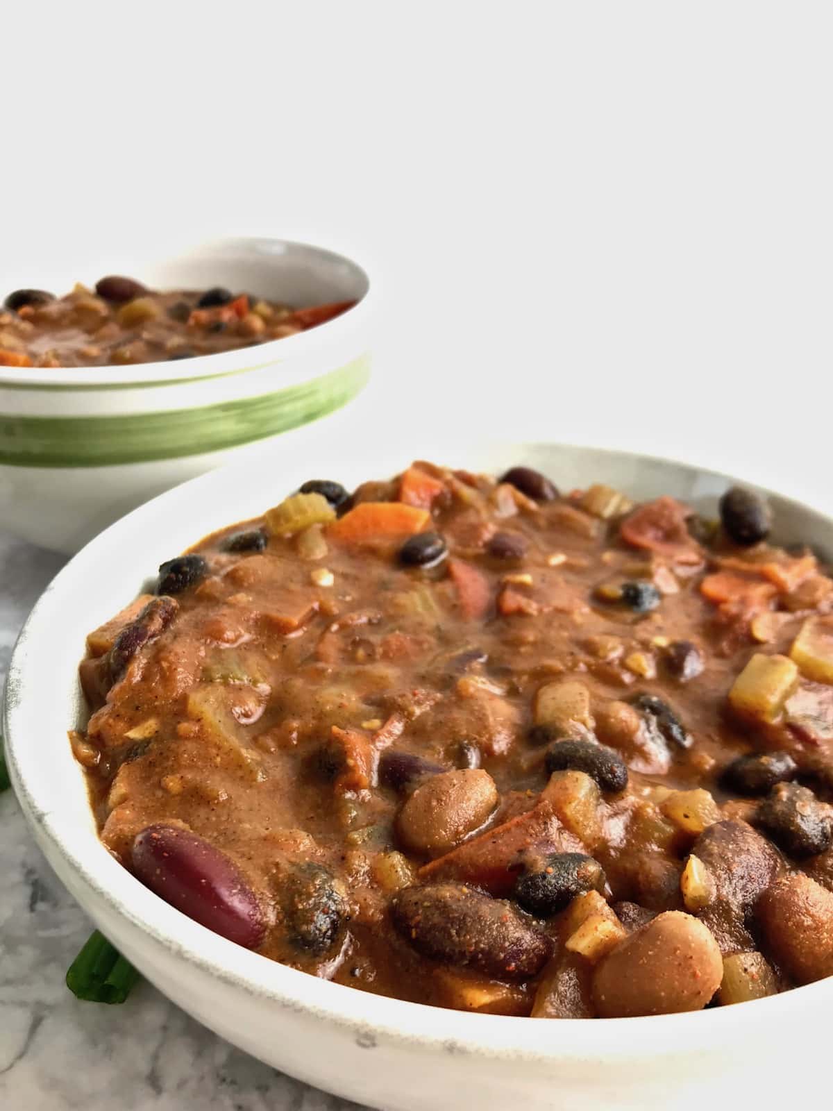 Close up of 3 bean chili in a bowl with another bowl of chili in the background.