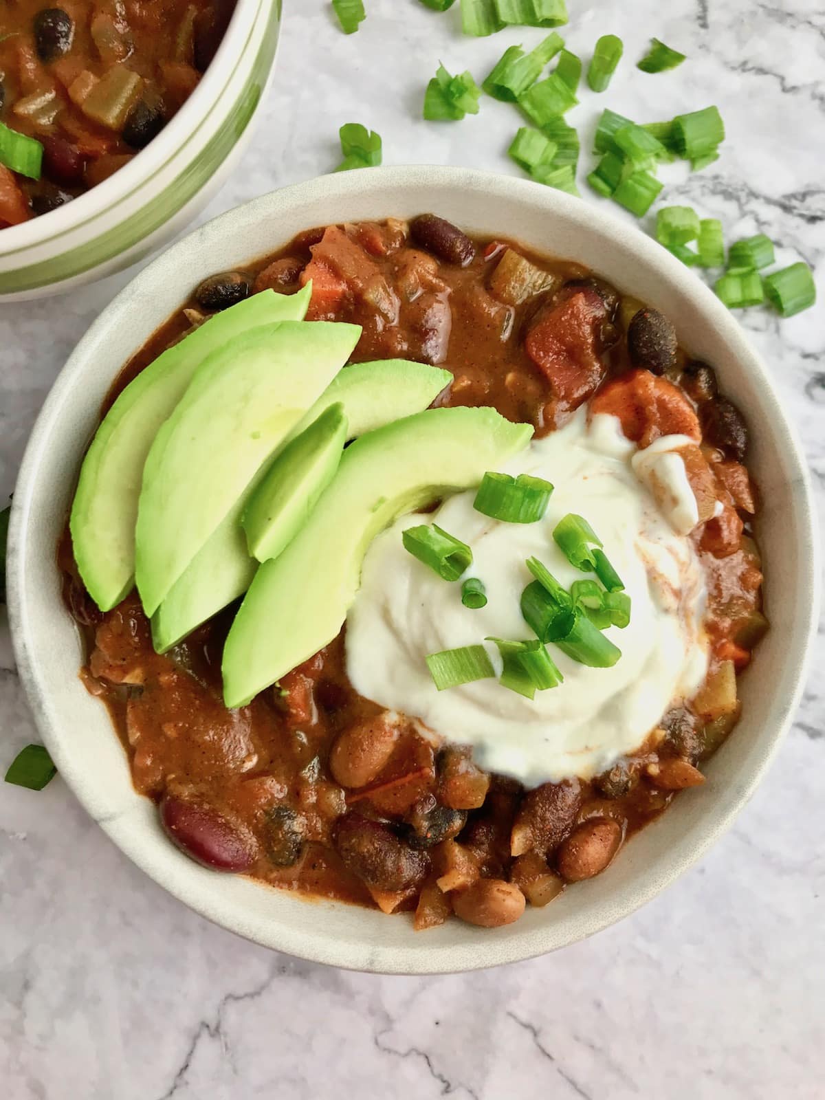 A bowl of 3 bean chili topped with tofu sour cream and avocado slices. 