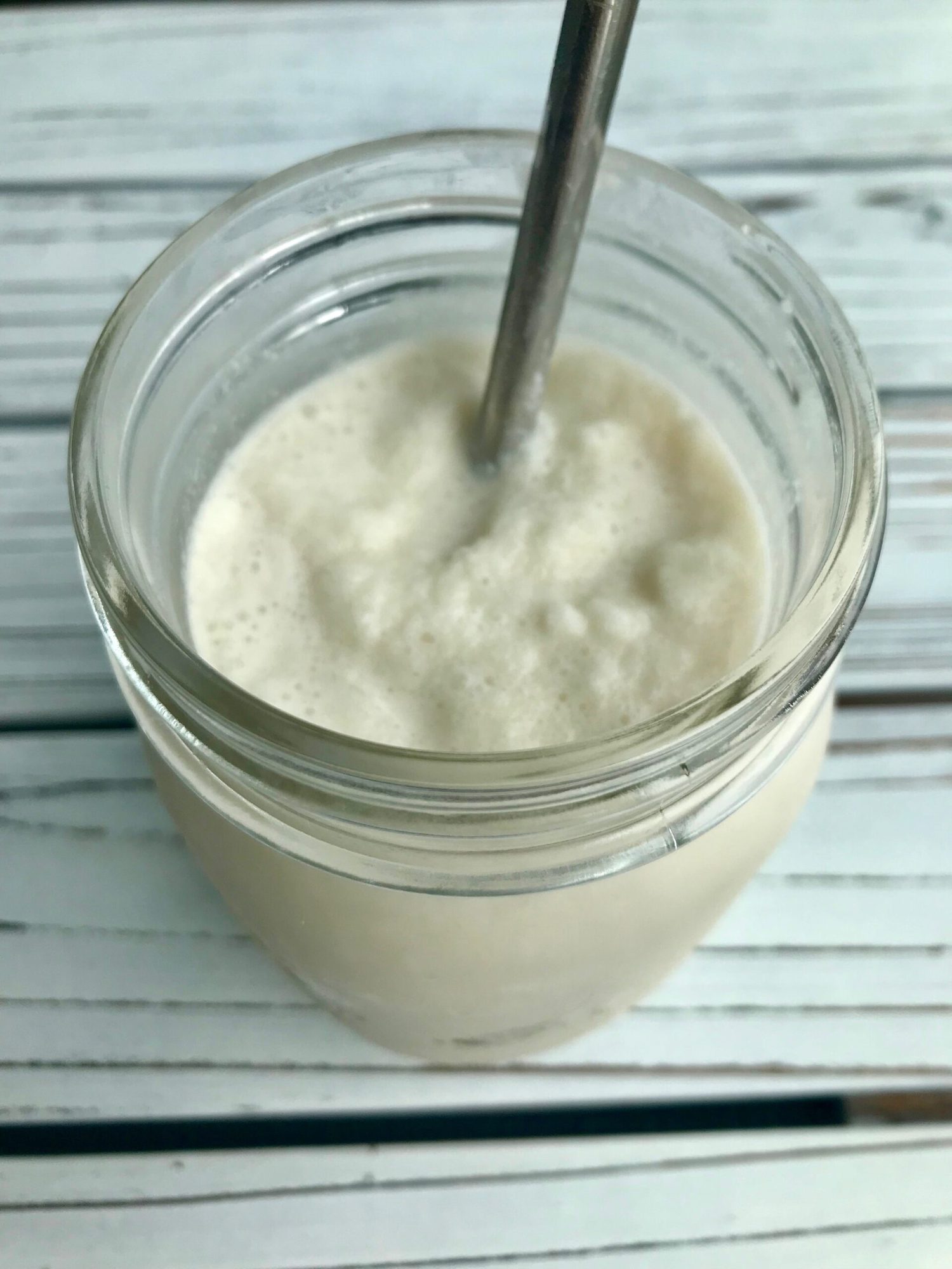 Vanilla coconut milkshake in a glass mason jar with a metal straw.