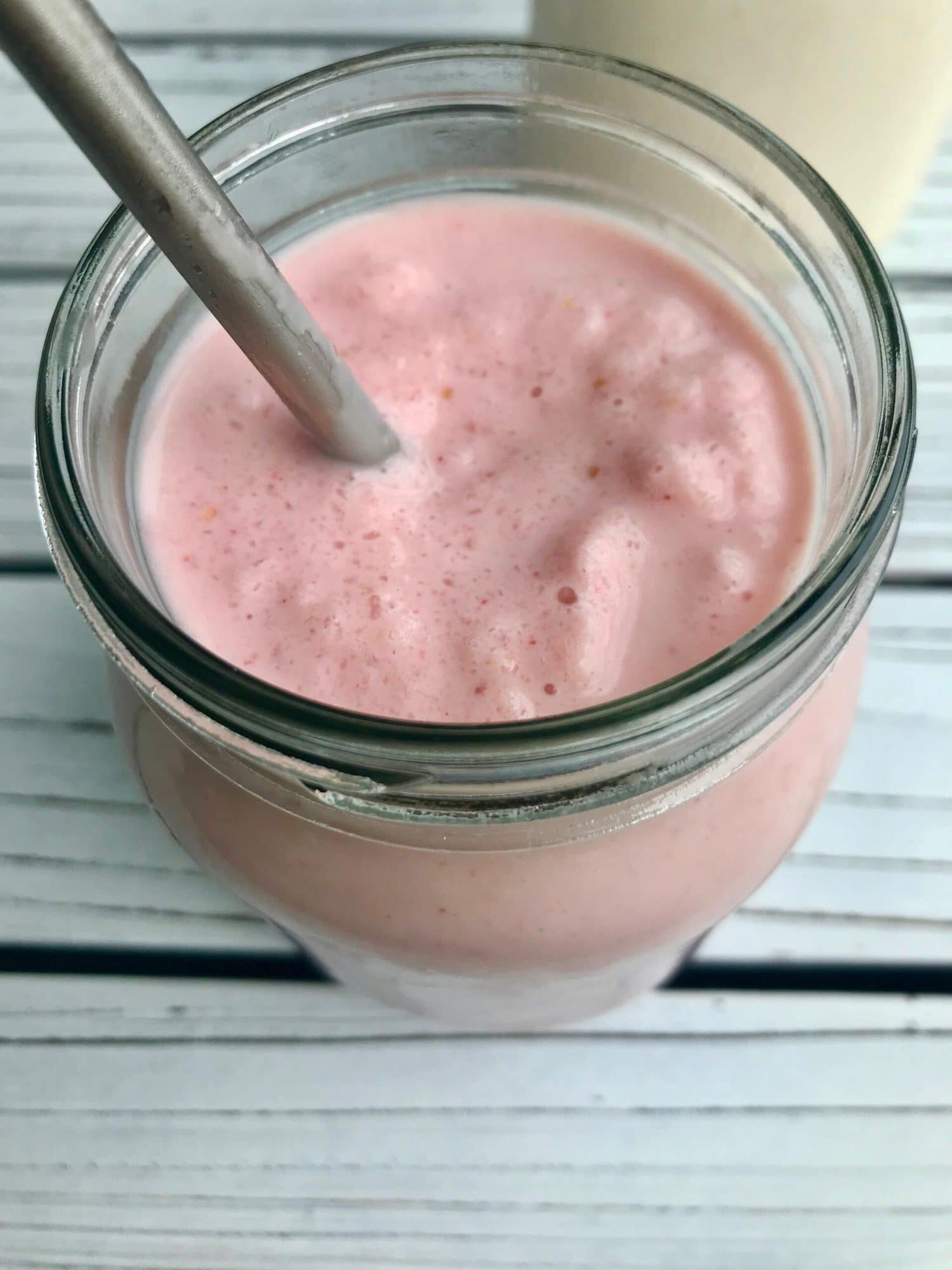 Strawberry coconut milkshake in a glass jar with a metal straw.