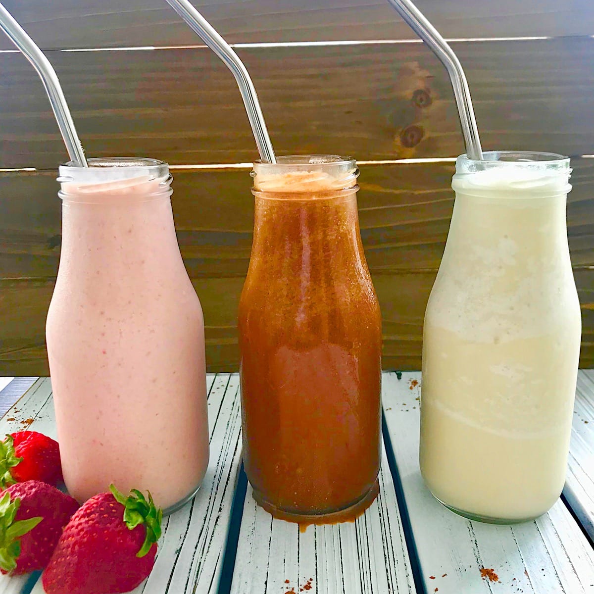 Three milkshakes in a row, starting with strawberry on the left, followed by chocolate and vanilla.