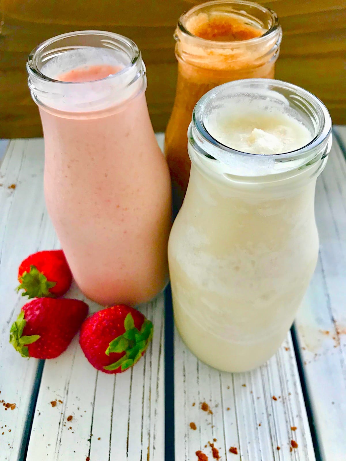 Three milkshakes in glass bottles, One strawberry, one vanilla, and one chocolate. 