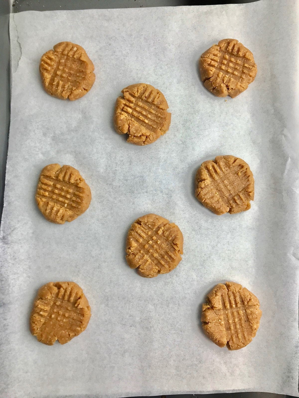 Peanut butter cookie dough flattened with a fork, laid out on a baking tray. 