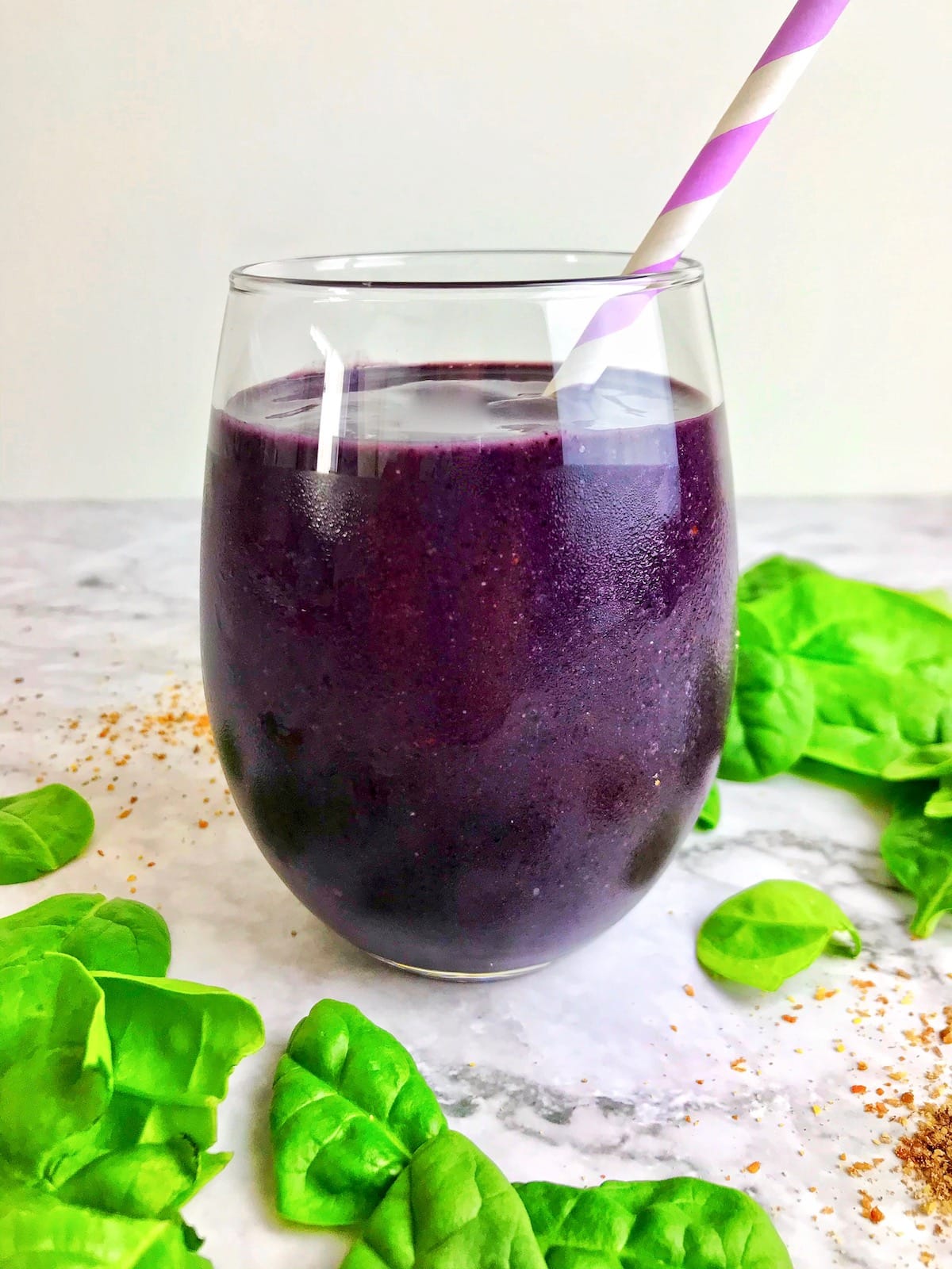 Purple blueberry spinach smoothie in a glass next to spinach and ground flaxseed on a table. 