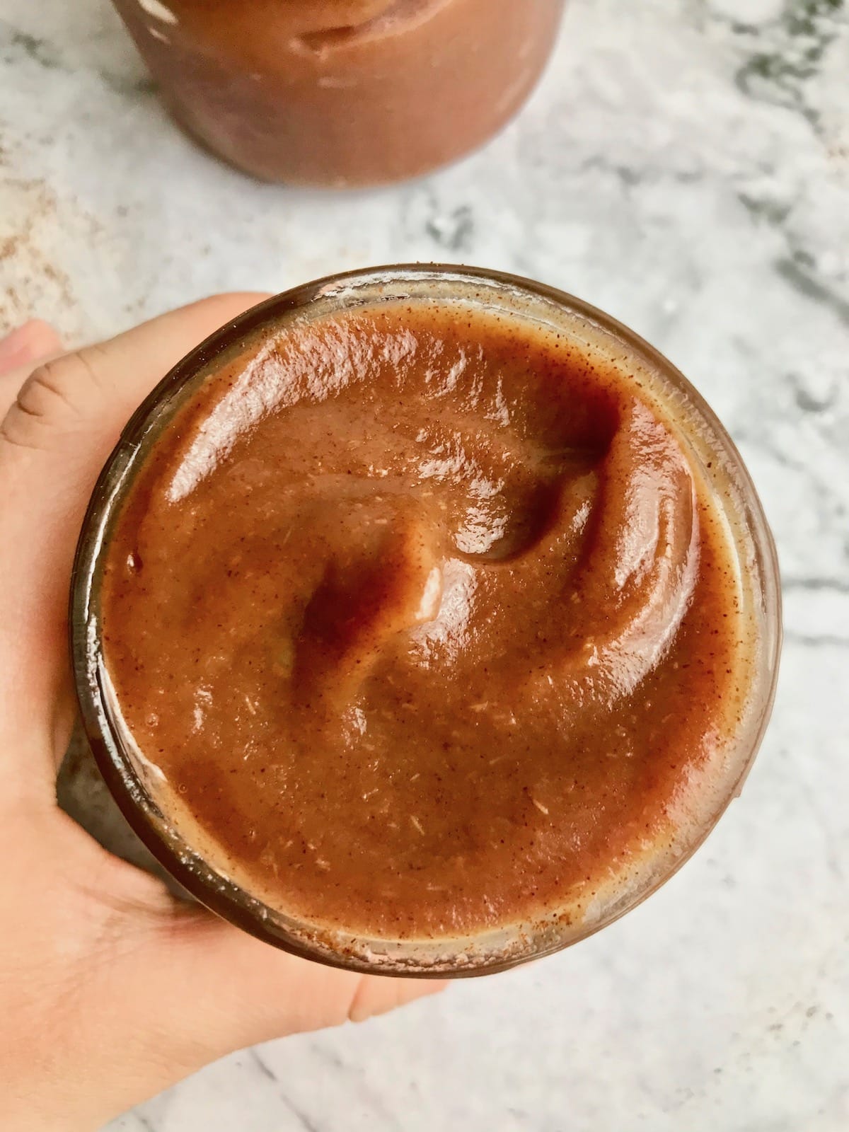 A hand holding a glass jar filled with apple butter.