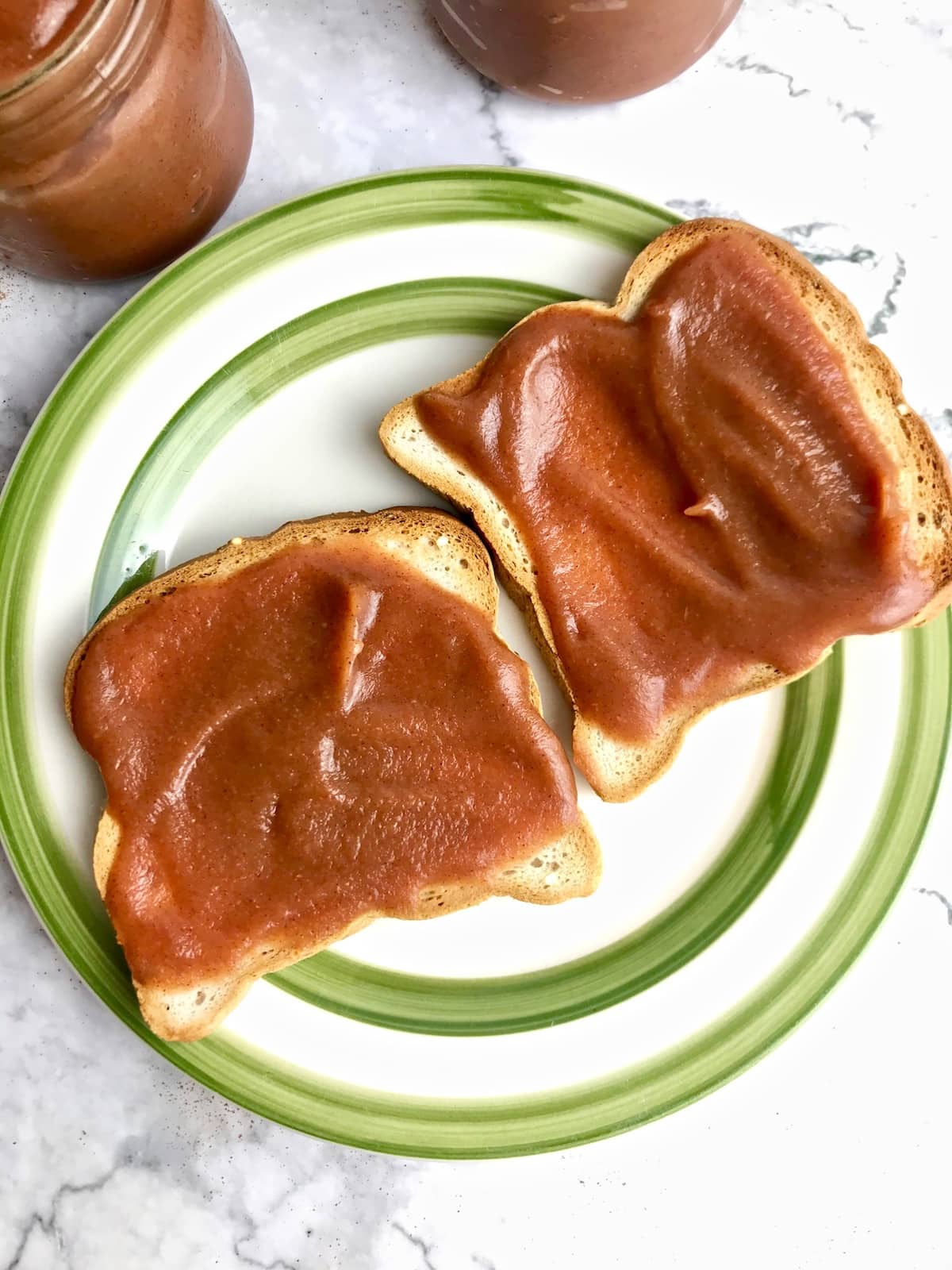 Two pieces of toast topped with apple butter on a white plate with a green rim.