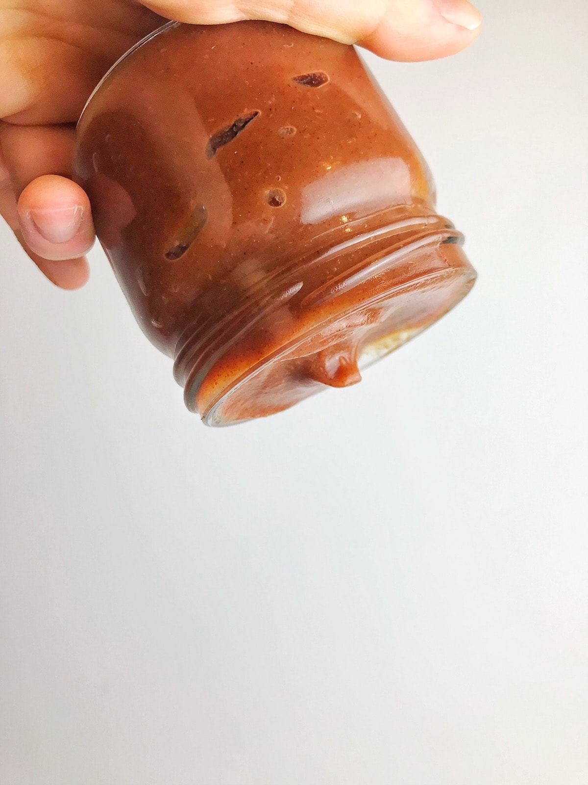 A hand holding a jar of apple butter upside down.
