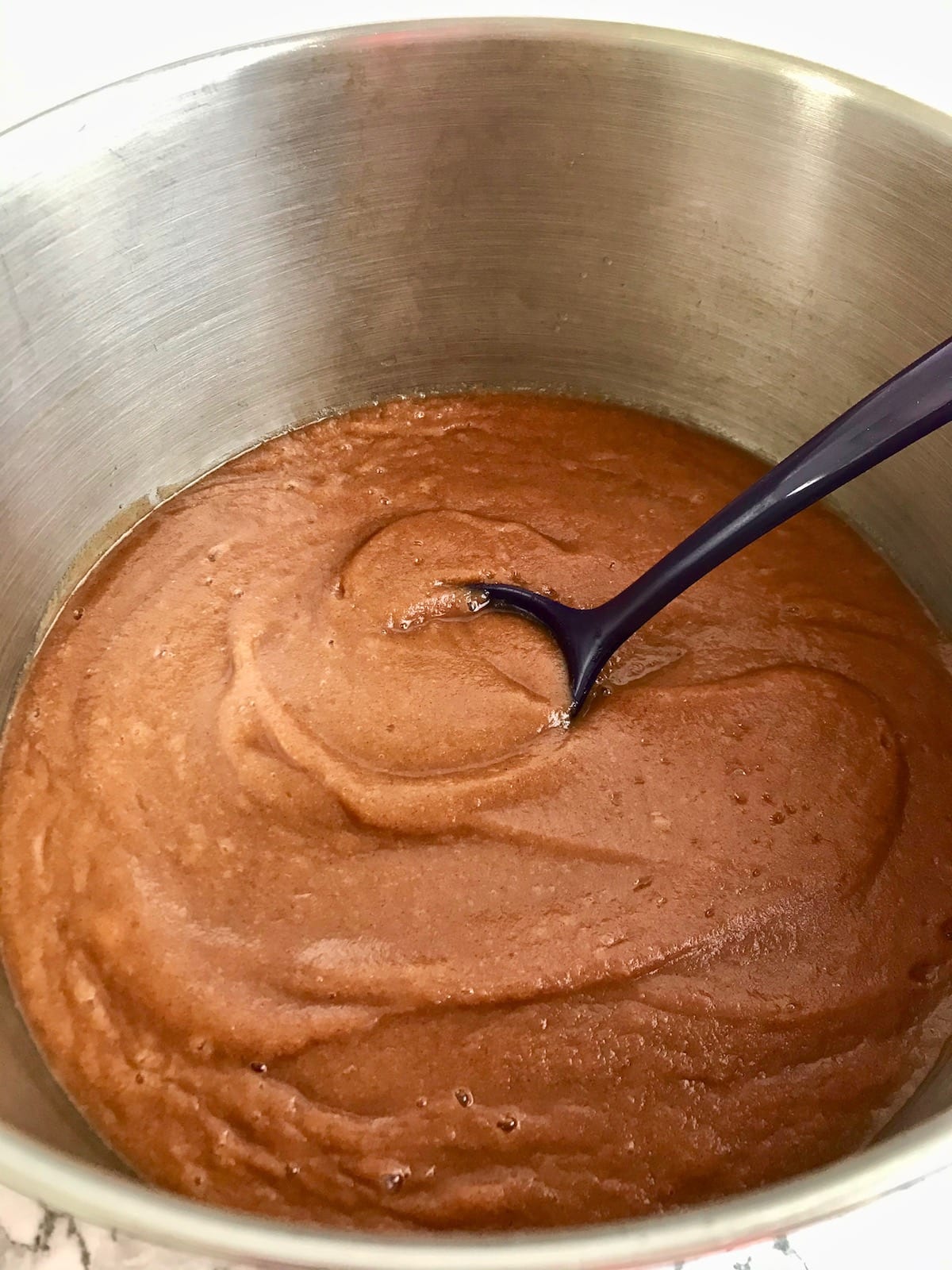 Blended apple butter in a pot with a purple spoon.