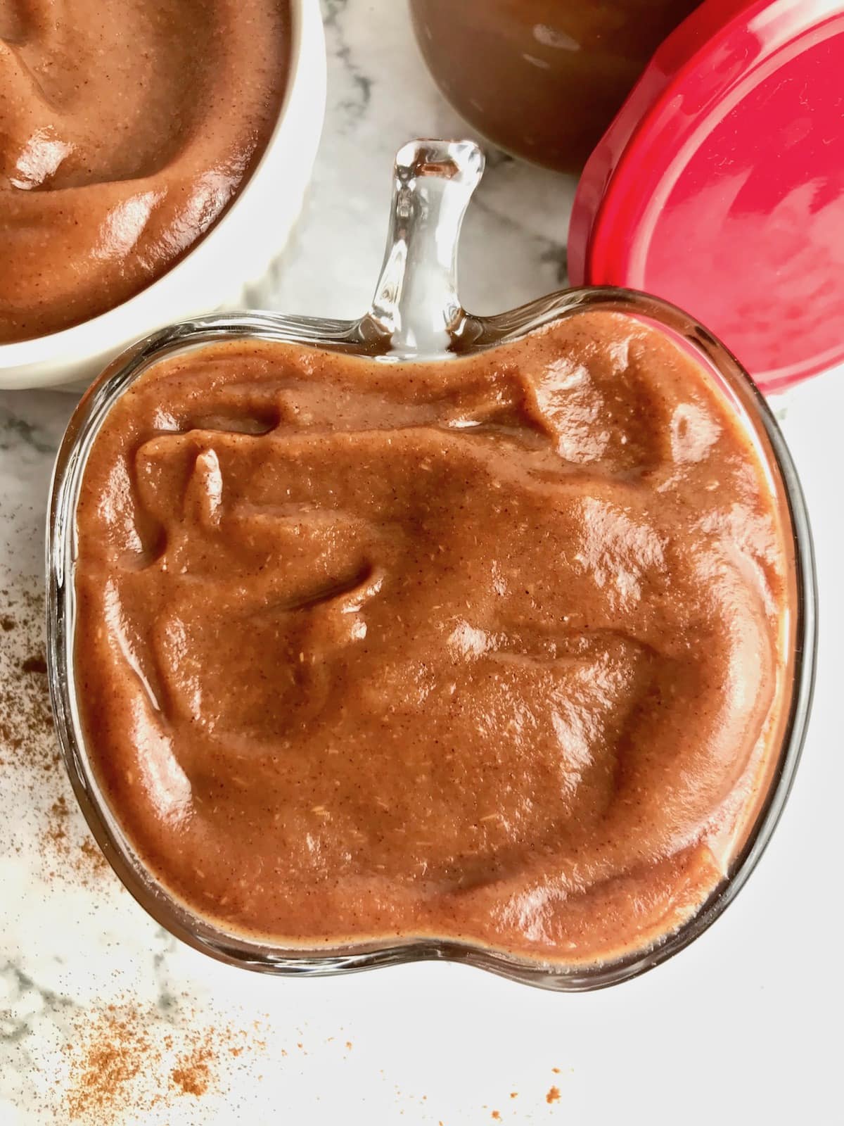 Thick apple butter in a glass dish with sprinkled cinnamon next to it.