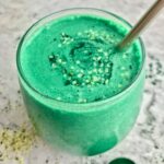 Turquoise spirulina smoothie in a stemless wine glass with a metal straw.