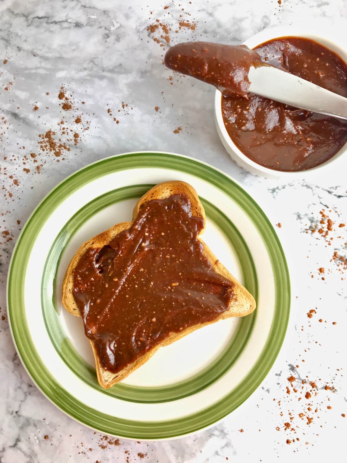 Chocolate peanut butter spread on toast next to a small container of chocolate peanut butter with a knife in it.