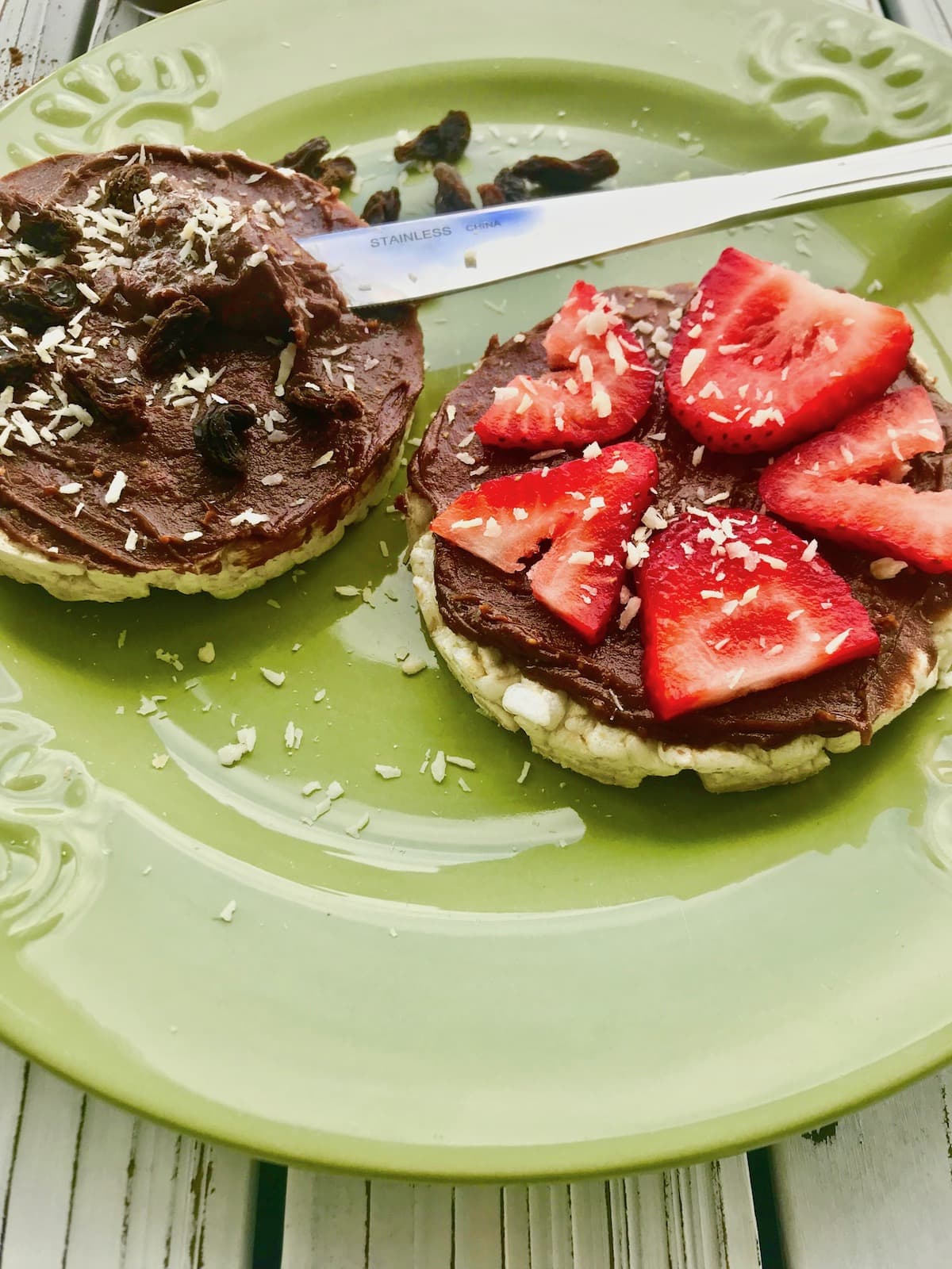 Chocolate peanut butter spread on rice cakes, topped with strawberries, raisins, and coconut flakes.