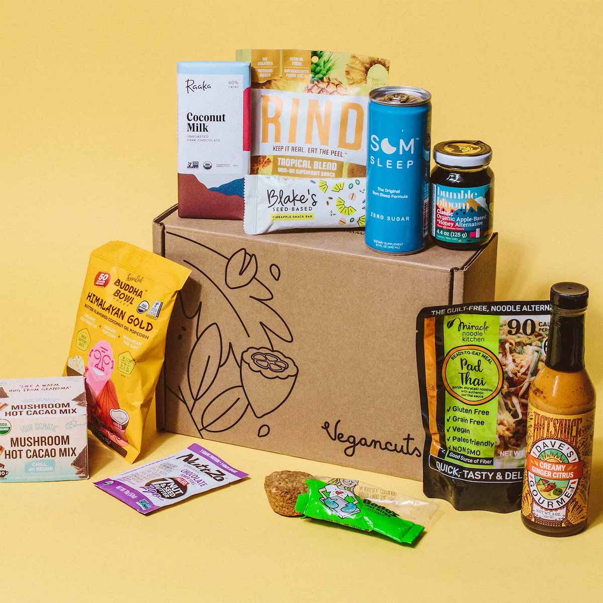 Several vegan snack items surrounding a cardboard box.