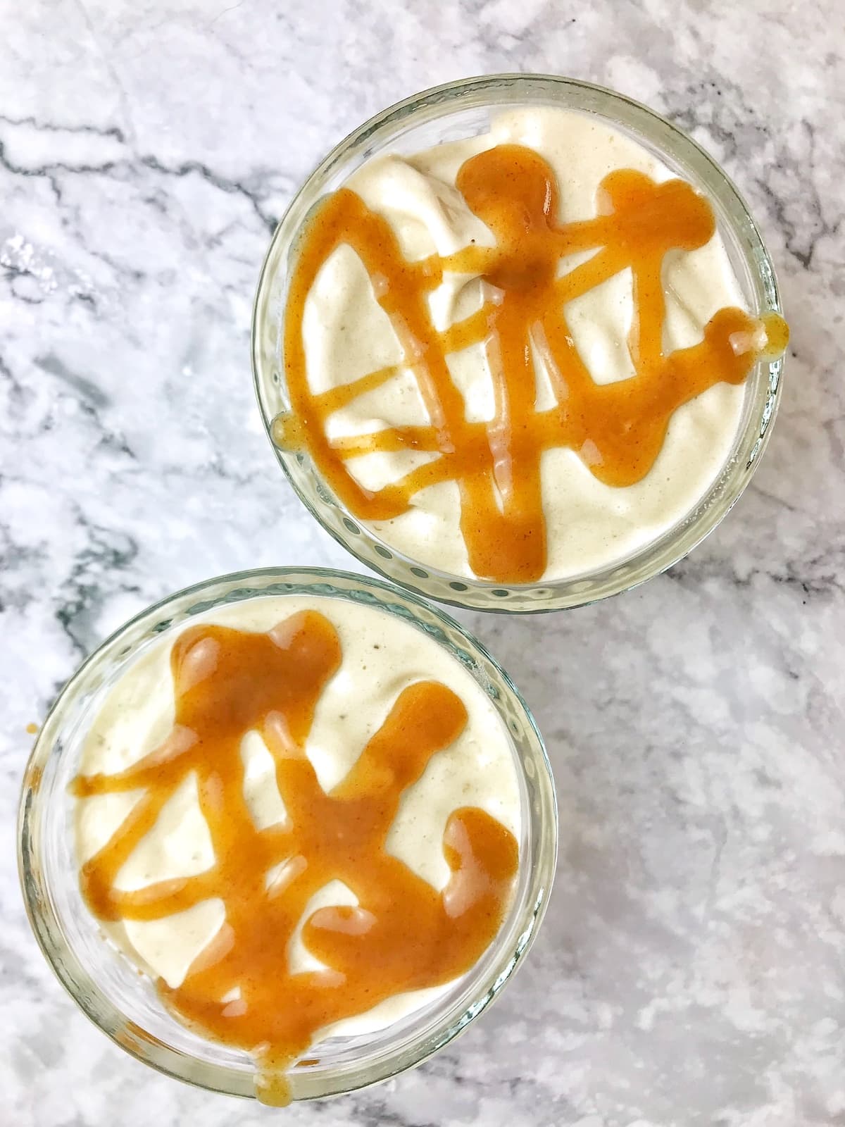 Two small bowls of banana swirl with caramel sauce on top.