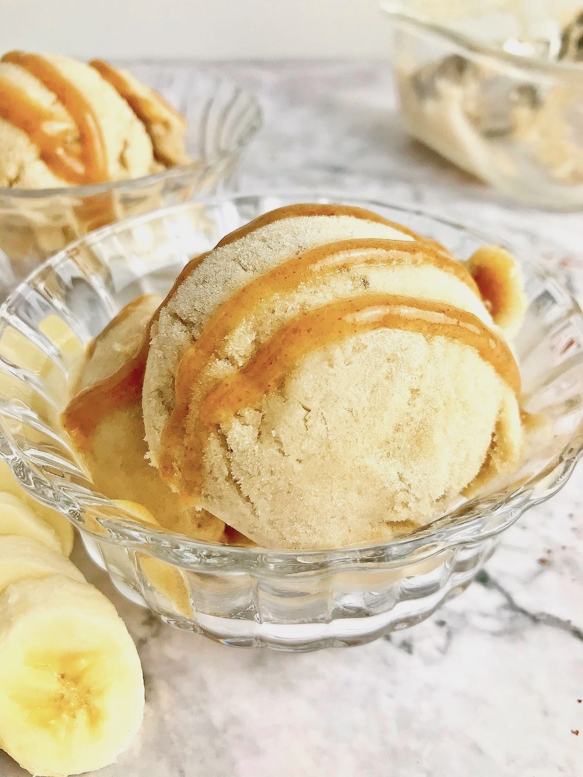 Banana nice cream in a clear bowl with caramel sauce drizzled on top.