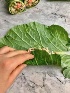 A hand rolling a collard leaf over a quinoa vegetable filling.