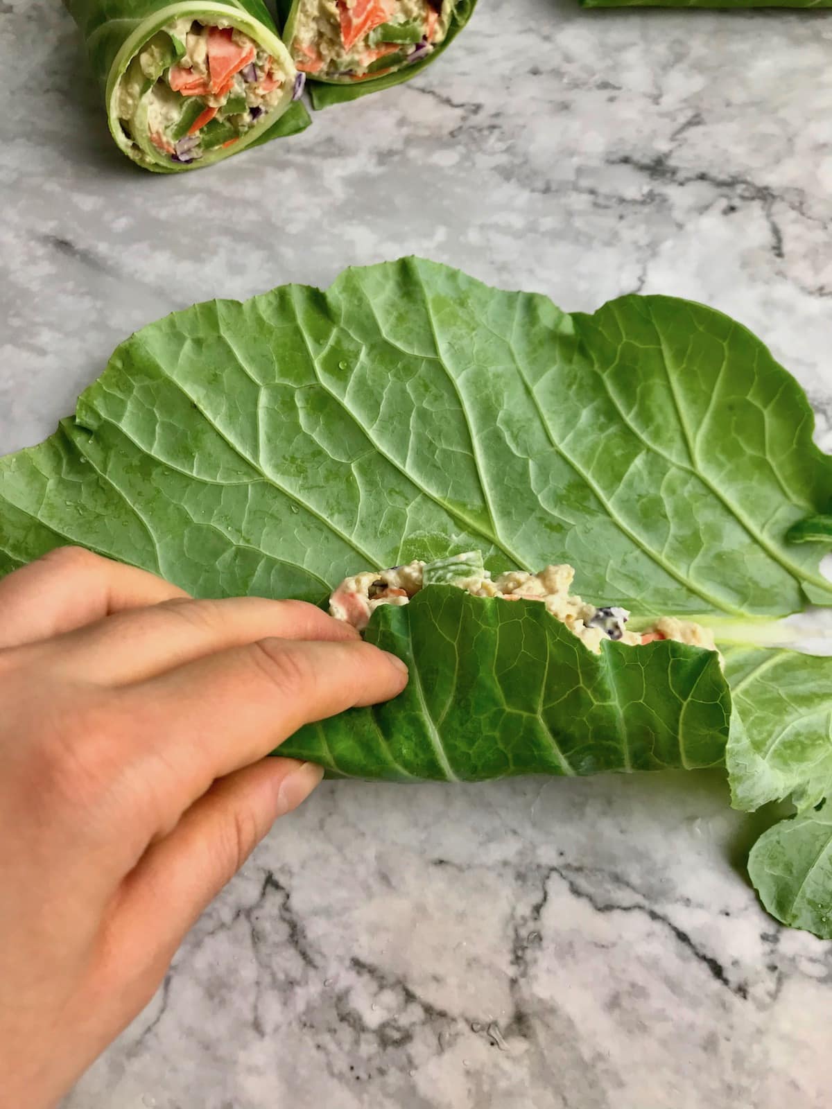 A hand rolling a collard leaf over the filling inside.