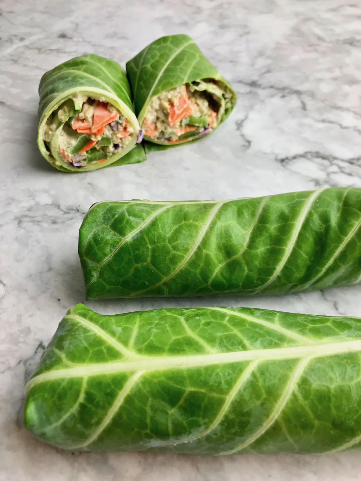 Two rolled up collard wraps and one cut in half collard wrap with a quinoa vegetable filling.