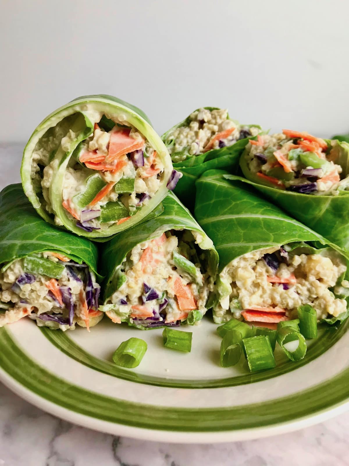 A pile of vegan collard green wraps on a plate, filled with quinoa and veggies.