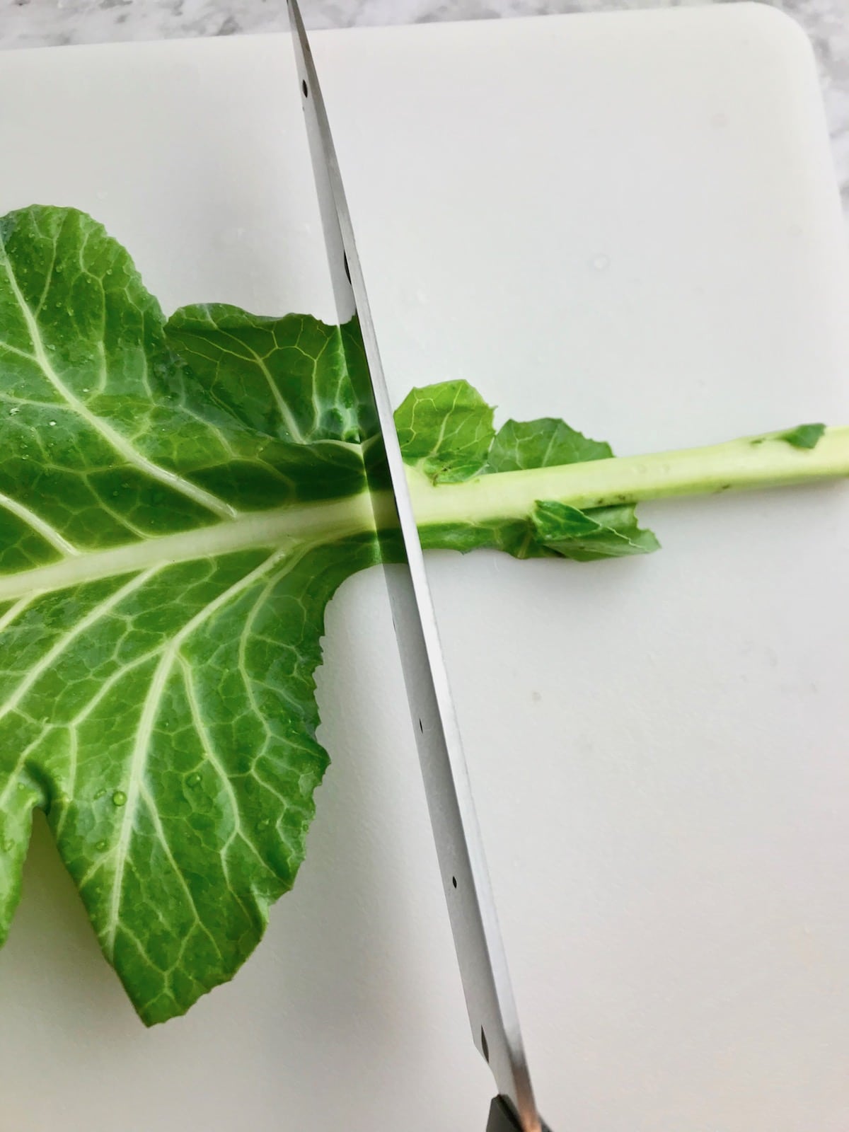 A knife cutting the stem off of a collard leaf.