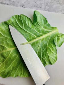 A knife slicing off the stem along the center of a collard leaf.