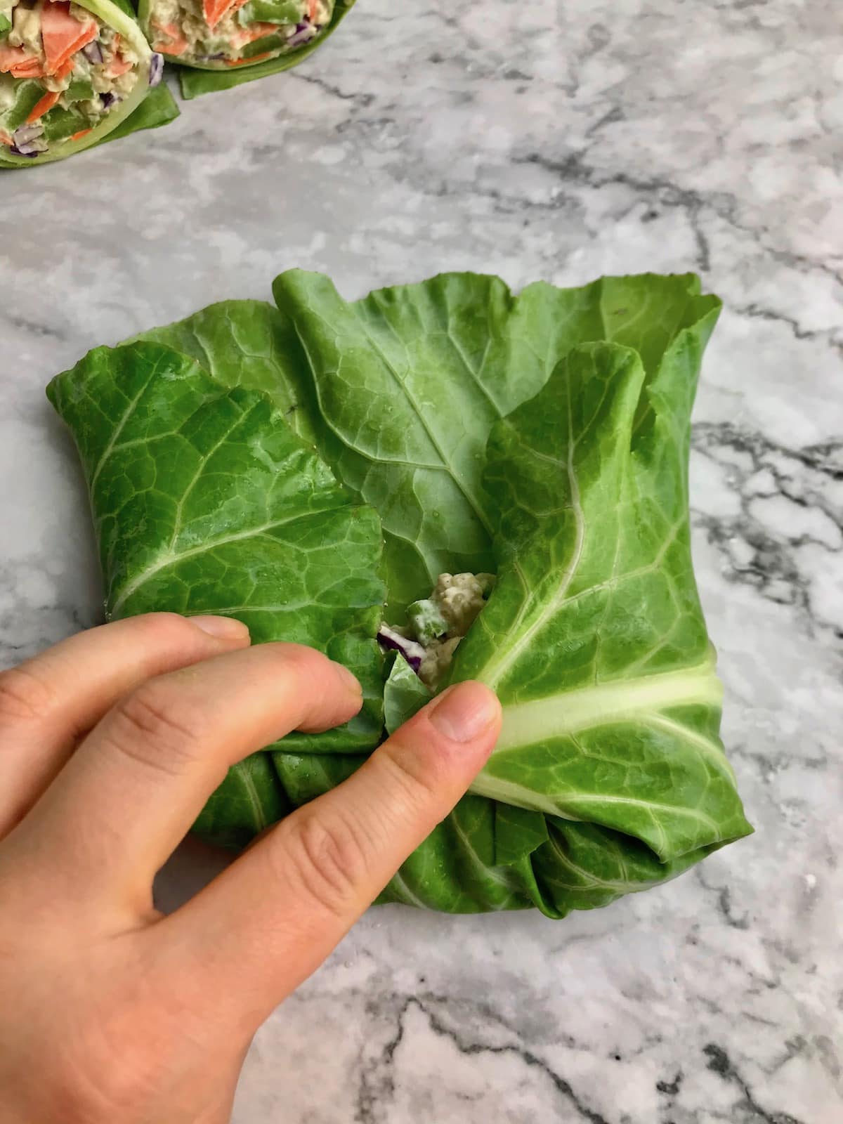 A hand holding the sides of a collard leaf wrapped around the filling.