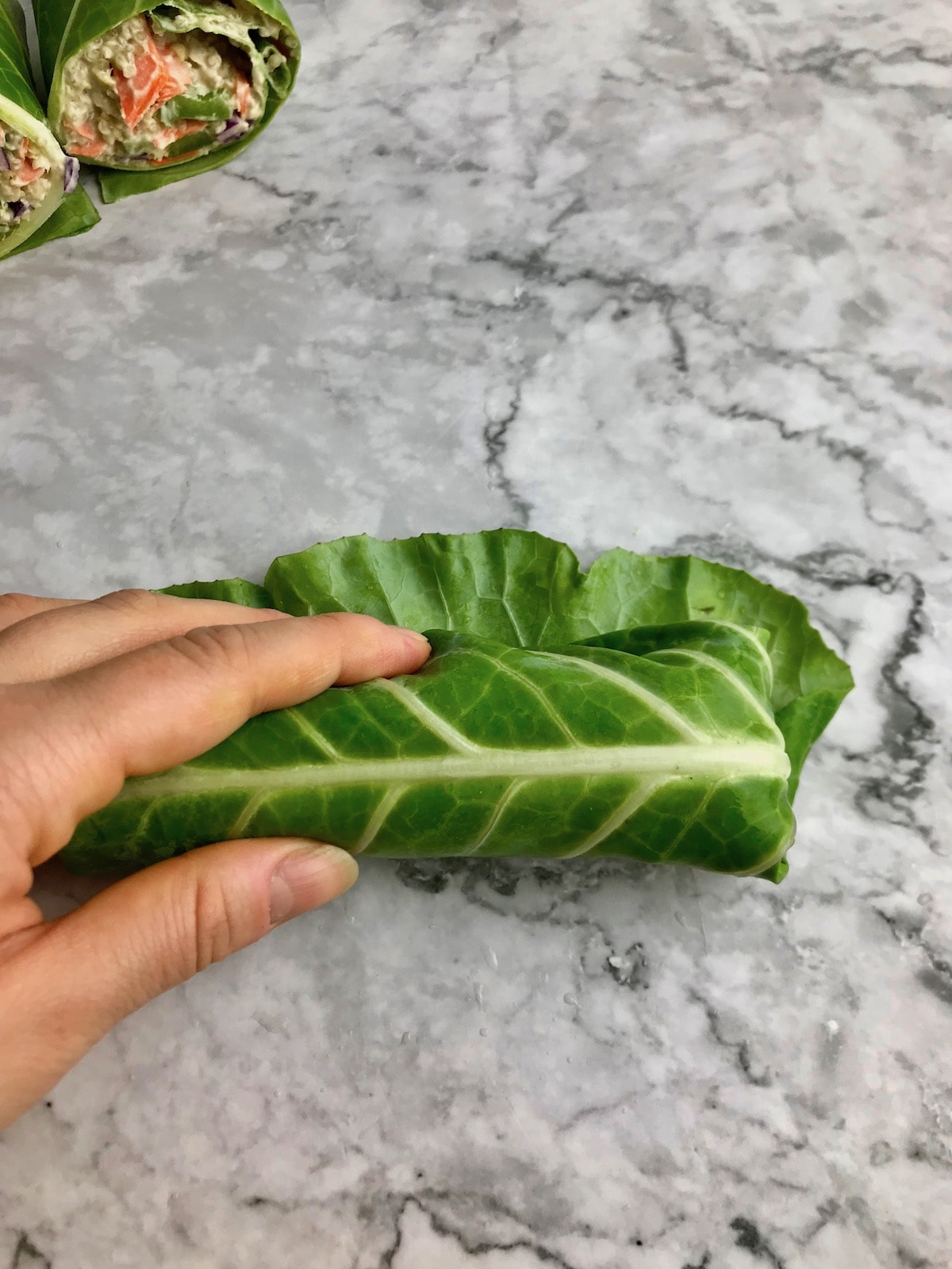 A hand holding a rolled up collard wrap on a table. 