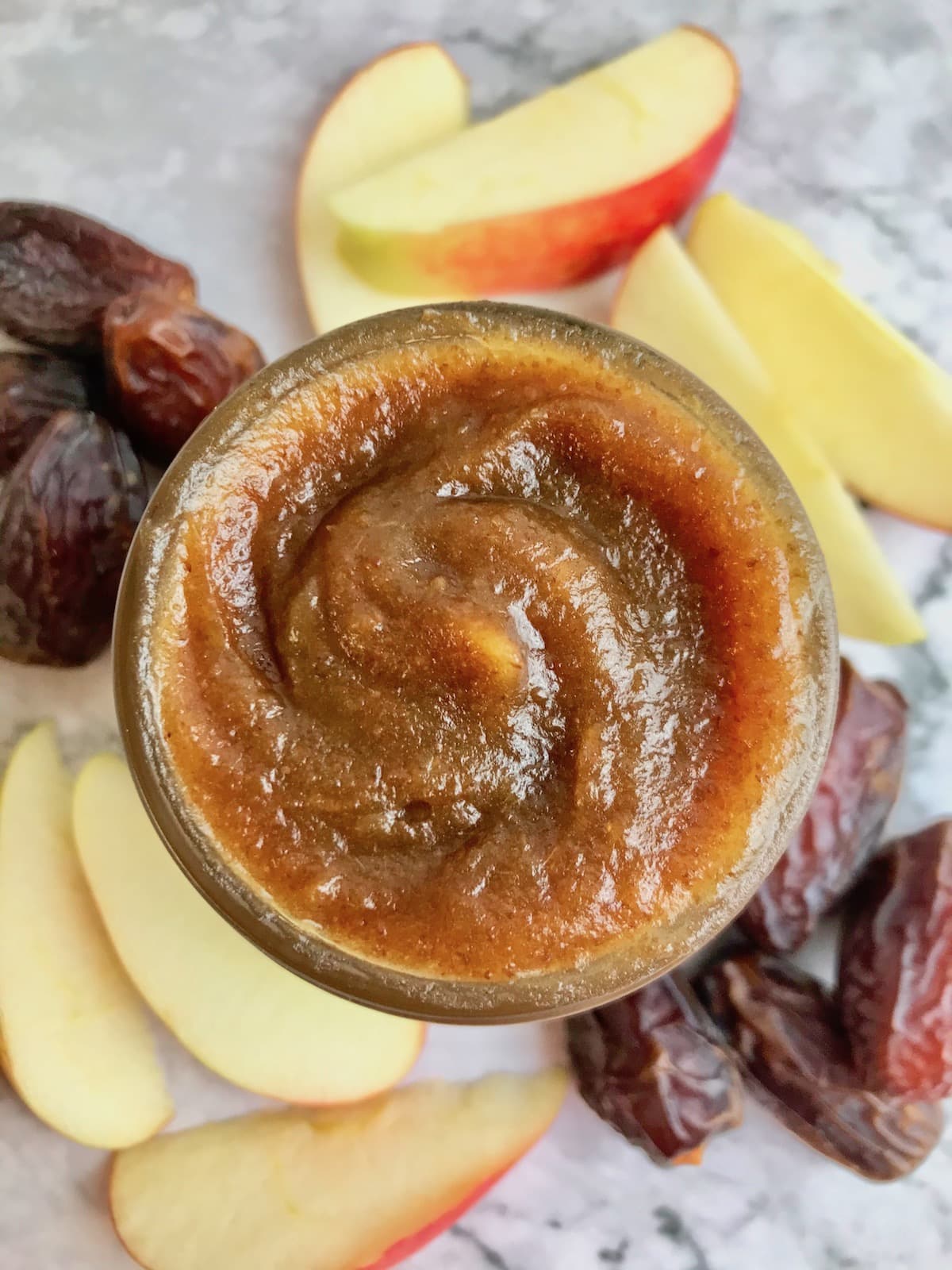 Overhead view of date caramel in a jar, surrounded by dates and apple slices.