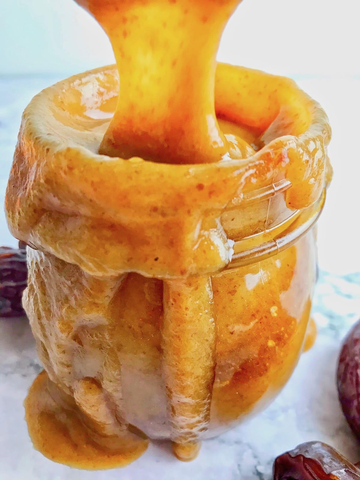 Vegan date caramel sauce dripping down a glass jar.