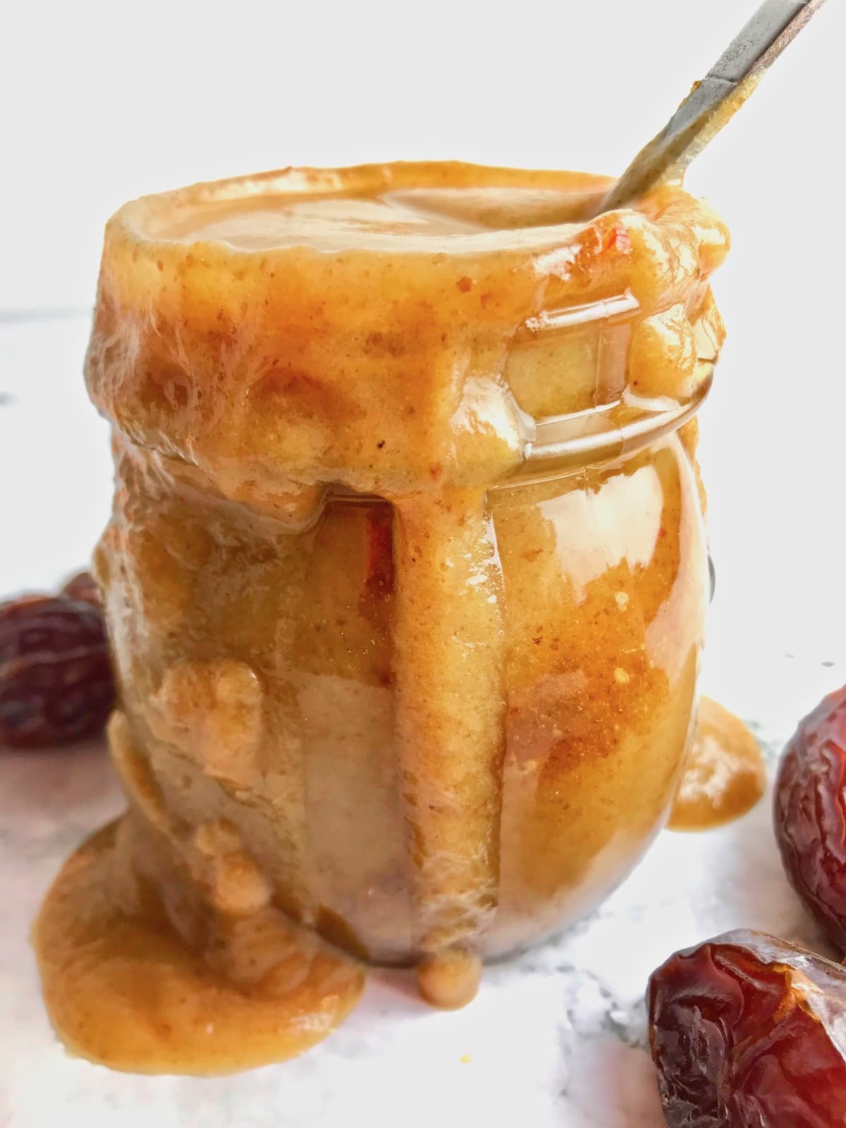 Vegan caramel sauce overflowing in a glass jar, surrounded by dates on a table. 