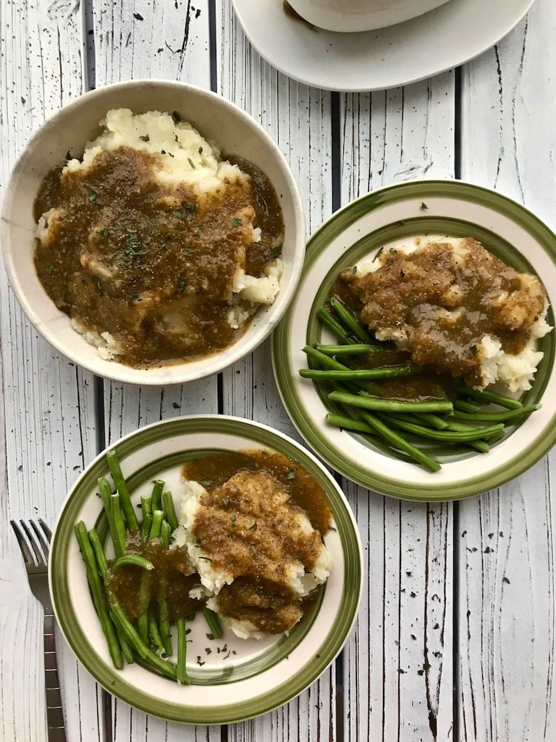 Mushroom gravy on three separate plates of mashed potatoes and green beans.