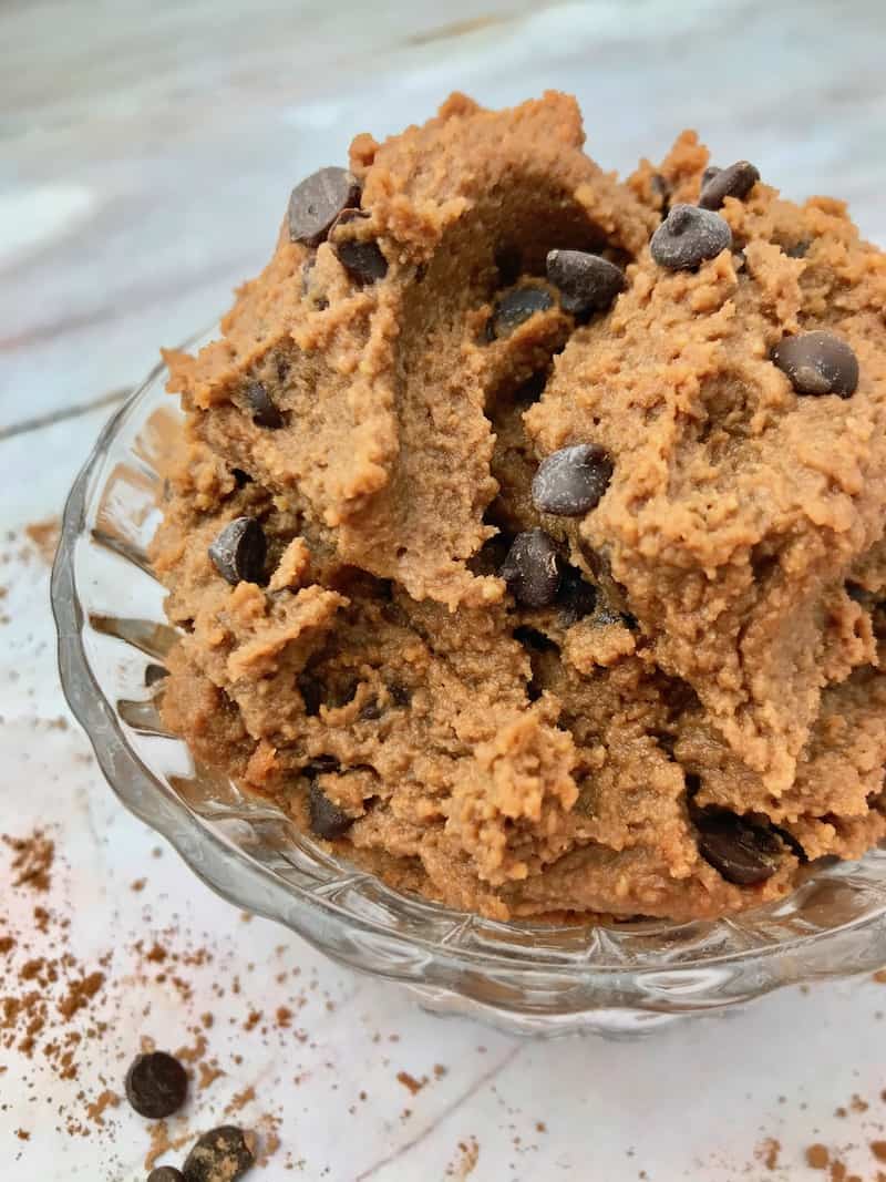 Chocolate chickpea cookie dough topped with chocolate chips in a small glass bowl.