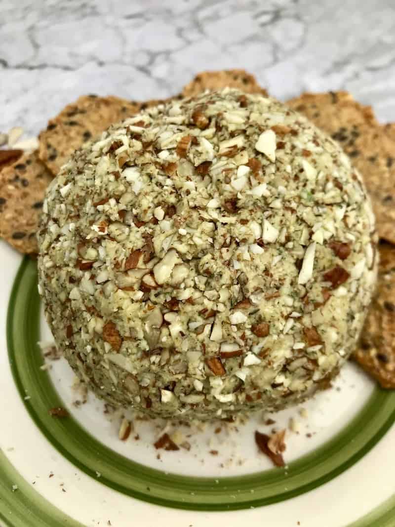 Cashew cheese ball covered in chopped nuts on a plate with crackers.