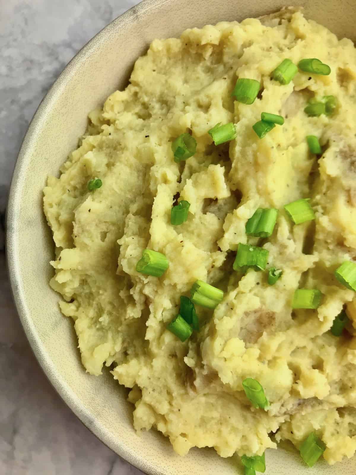 Half a bowl of mashed potatoes with chopped green onion on top.