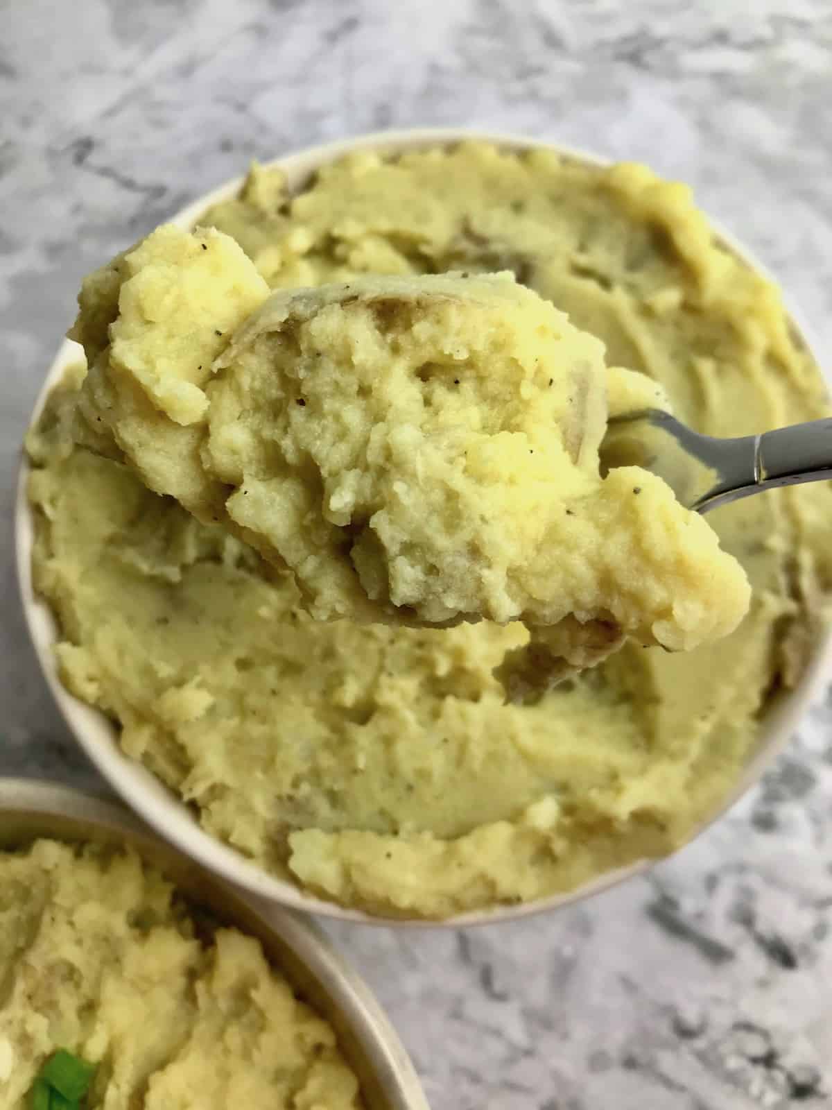 A spoonful of mashed potatoes over a bowl of mashed potatoes.