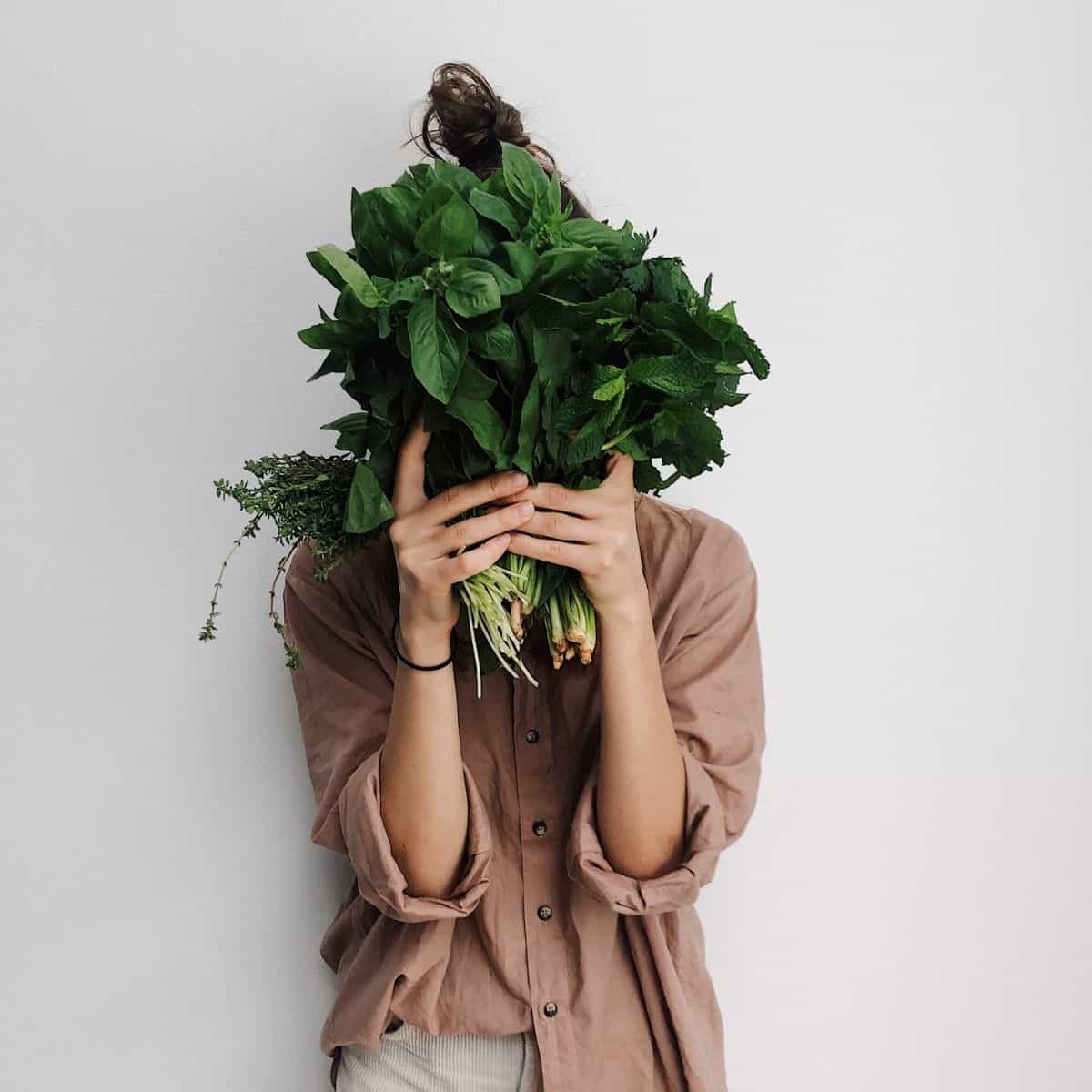 A woman holding leafy green vegetables in front of her face.