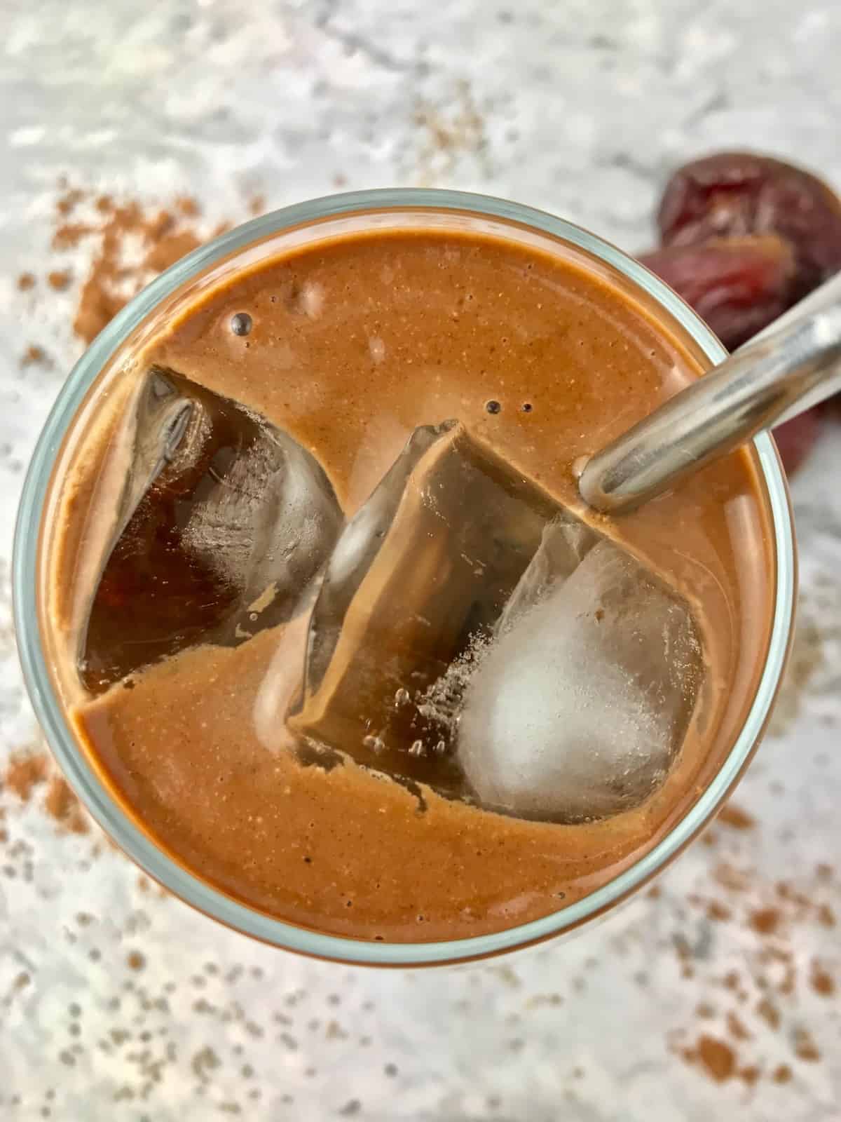 Overhead view of a glass of a banana coffee smoothie with ice in it.