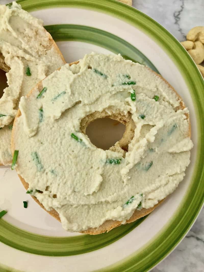 A bagel with onion cream cheese on a green and white plate.