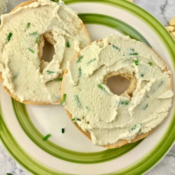 A bagel with cashew cream cheese on a green and white plate.