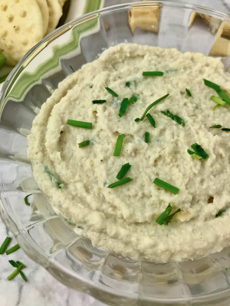 Cashew cream cheese topped with chopped chives in a glass bowl.