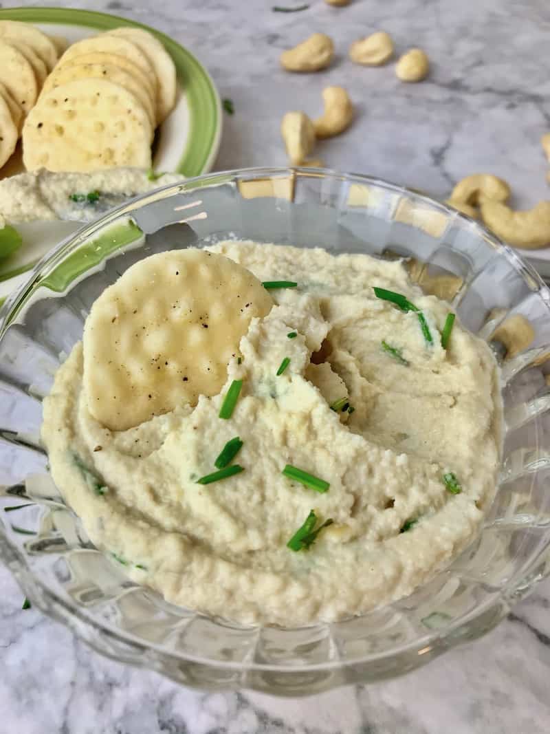 A bowl of cashew cream cheese with a cracker in it.